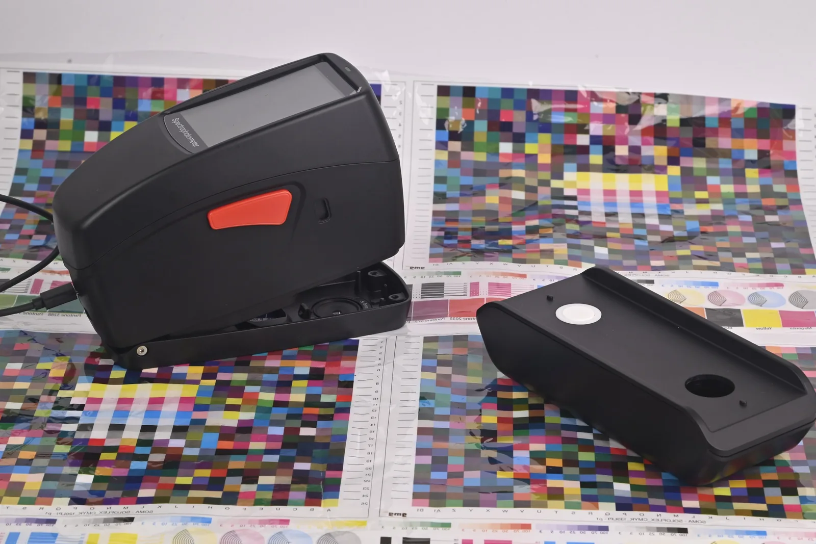 SpectroFit spectrodensitometer beside its calibration base on printed CMYK test charts